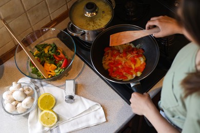 Woman cooking vegetables in frying pan on stove indoors, above view