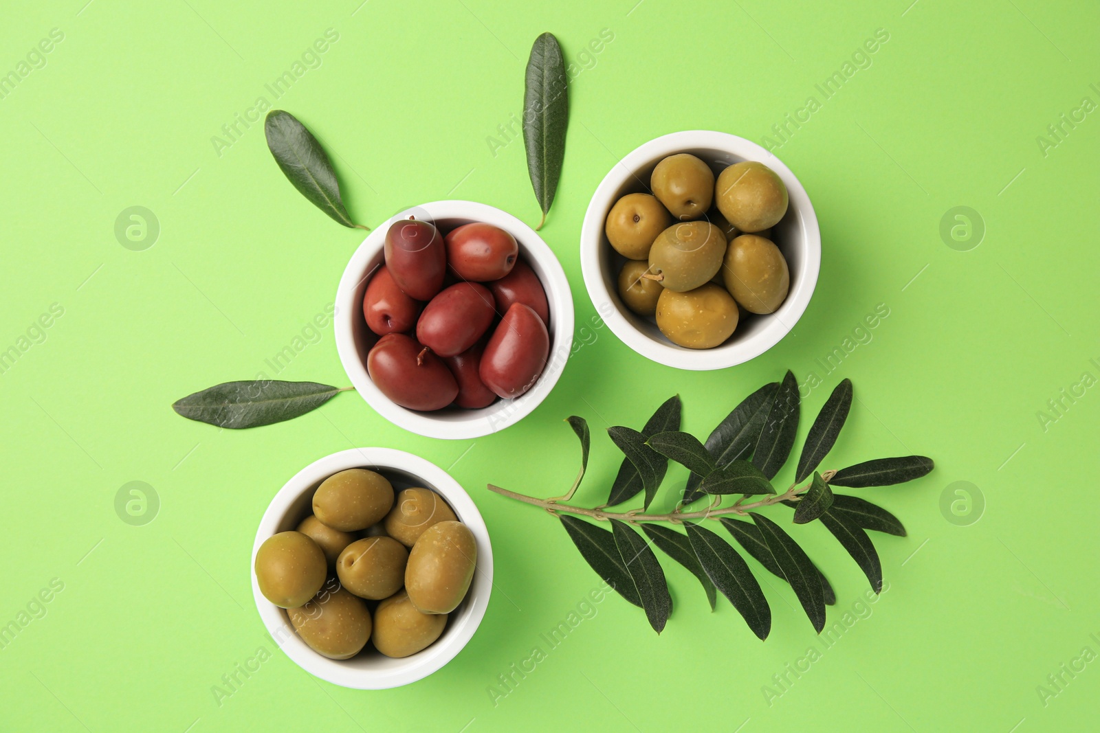 Photo of Different fresh olives and leaves on light green background, flat lay