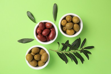 Different fresh olives and leaves on light green background, flat lay