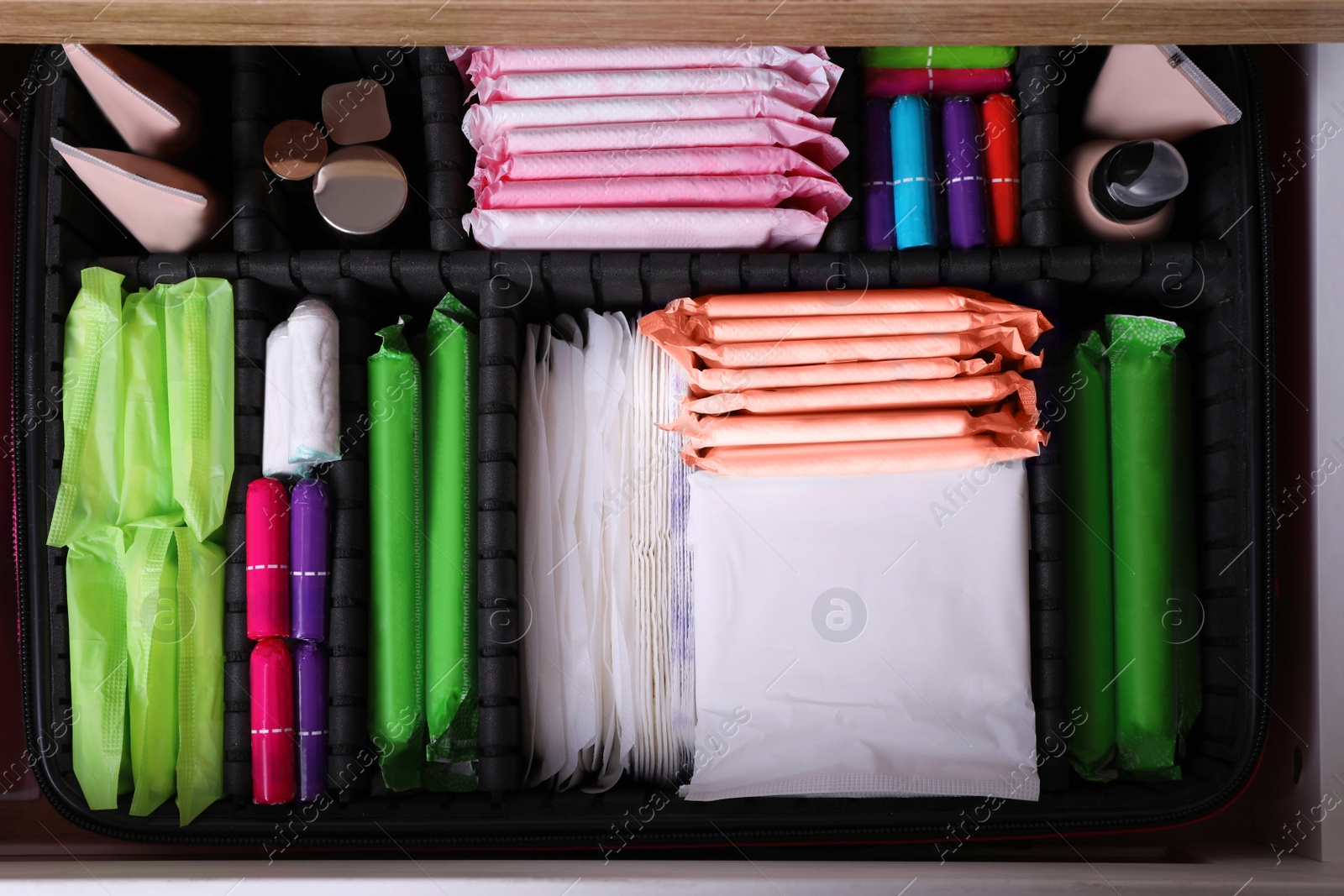 Photo of Open cabinet drawer with menstrual pads, tampons, makeup and skin care products, top view