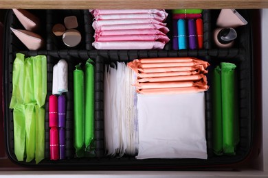 Open cabinet drawer with menstrual pads, tampons, makeup and skin care products, top view