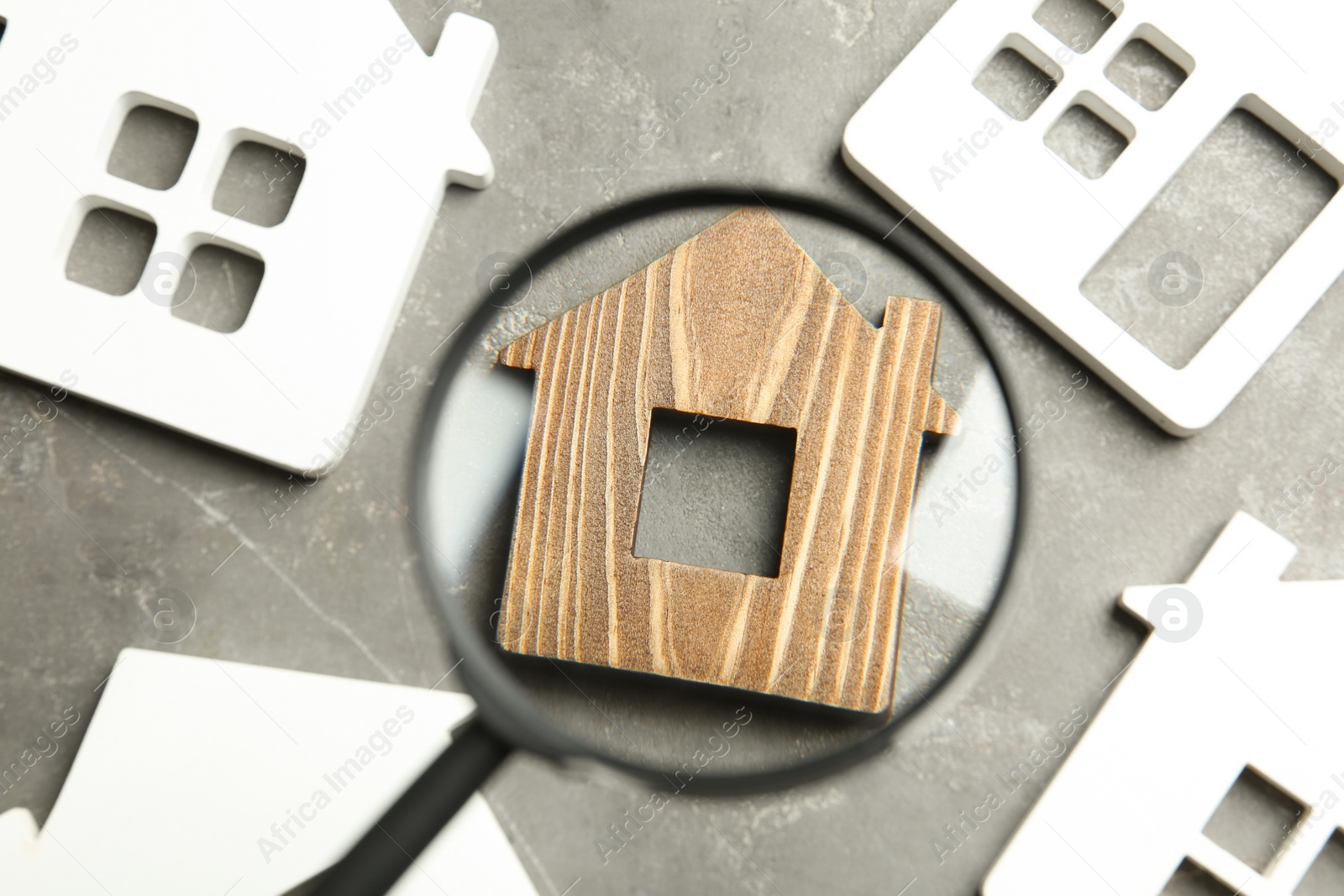 Photo of Magnifying glass and house models on grey stone table. Search concept