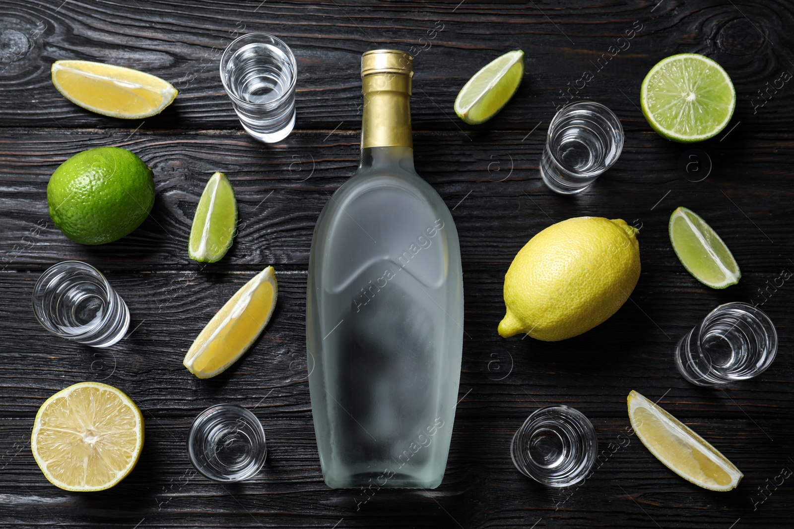 Photo of Bottle of vodka, citrus fruits and shot glasses on black wooden table, flat lay. Space for design