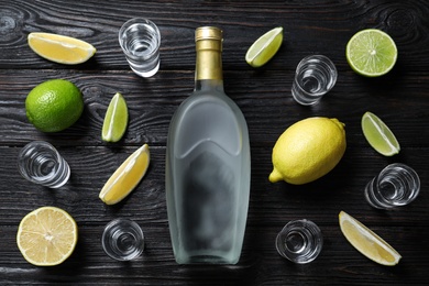 Bottle of vodka, citrus fruits and shot glasses on black wooden table, flat lay. Space for design