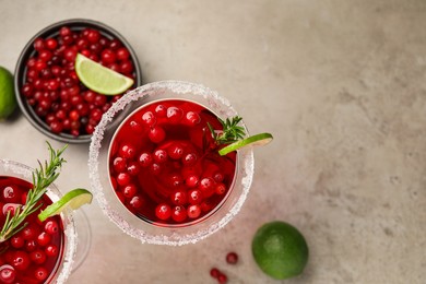 Tasty cranberry cocktail with rosemary and lime in glasses on grey table, flat lay. Space for text