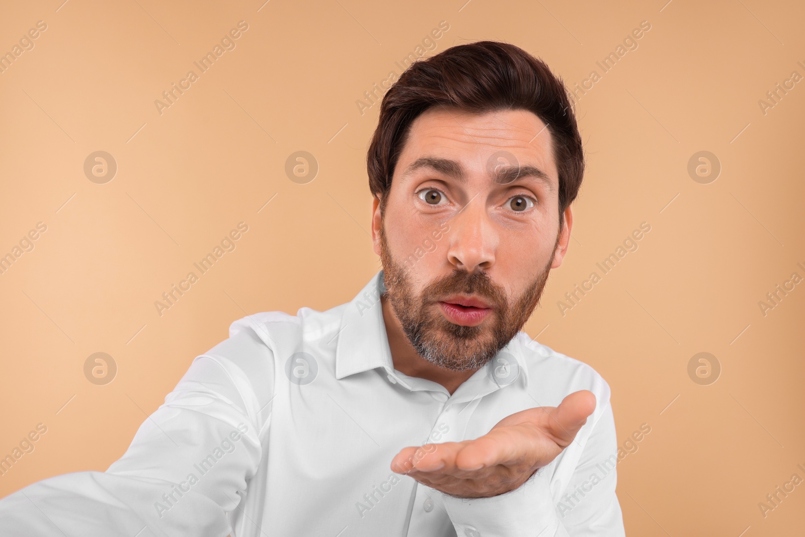 Photo of Bearded man taking selfie and blowing kiss beige background