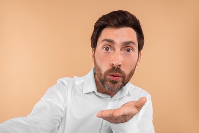Photo of Bearded man taking selfie and blowing kiss beige background