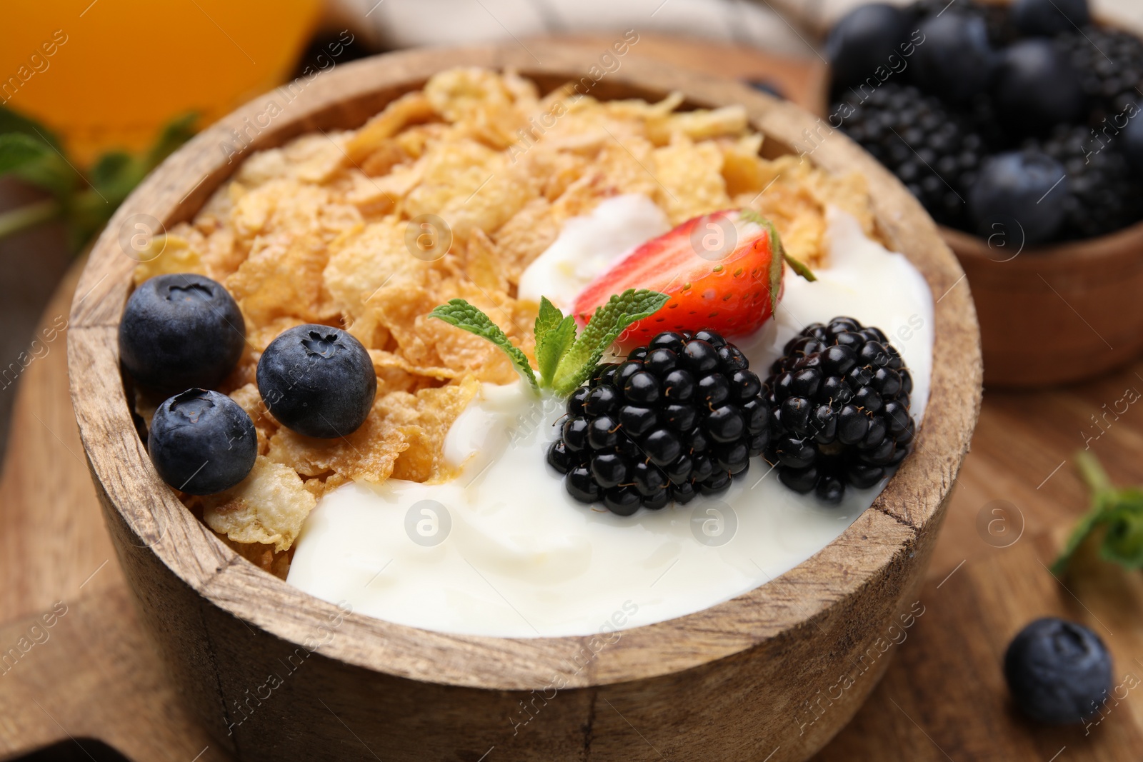 Photo of Delicious crispy cornflakes, yogurt and fresh berries in bowl on wooden board, closeup. Healthy breakfast
