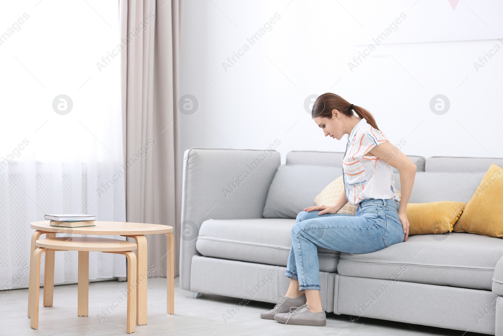 Photo of Young woman suffering from hemorrhoid on sofa at home