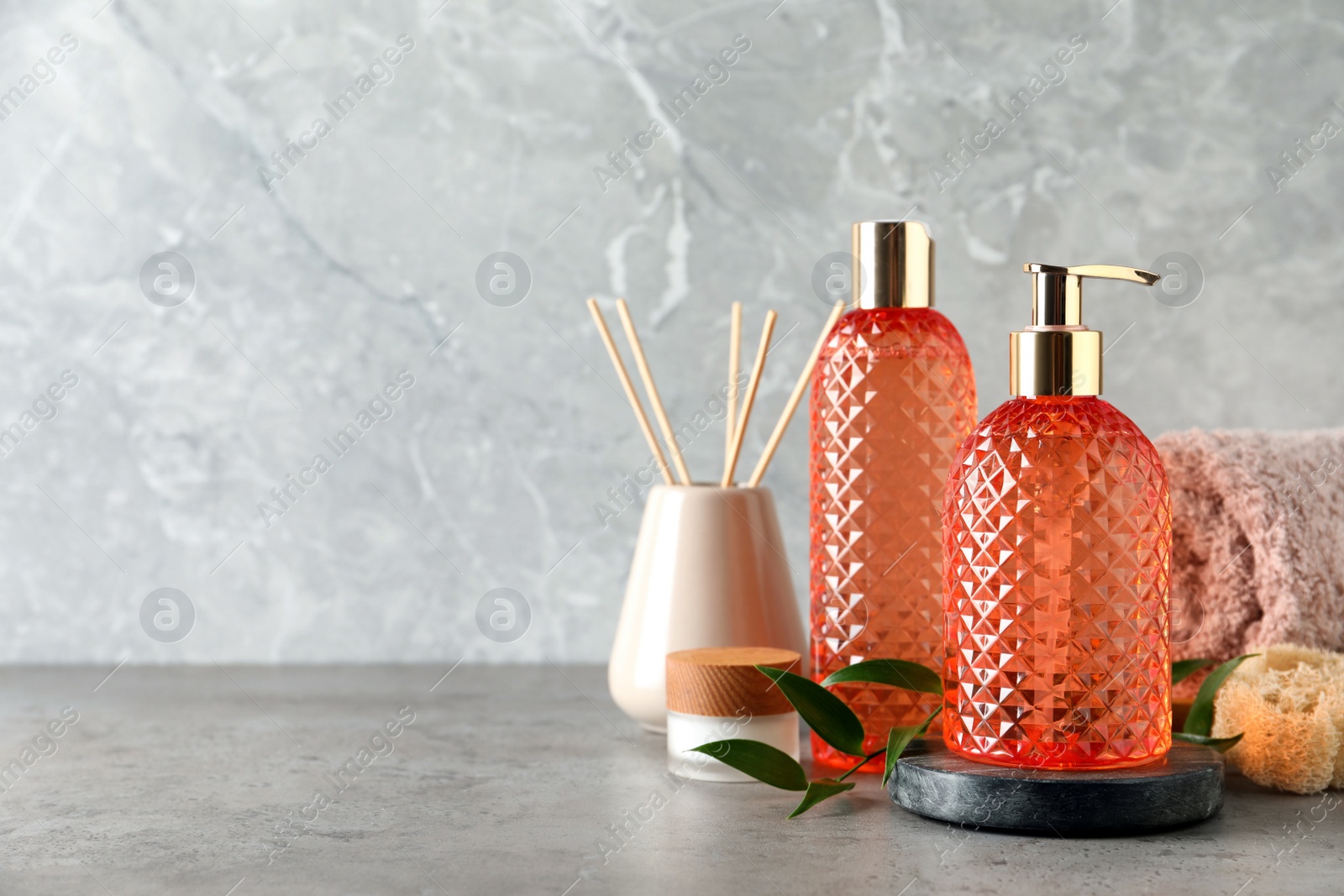 Photo of Stylish dispenser with liquid soap and other bathroom amenities on grey table, space for text