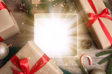 Image of Beautiful Christmas gift with magic light on wooden background, flat lay