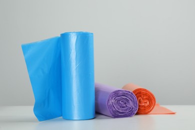 Rolls of different color garbage bags on table against light background