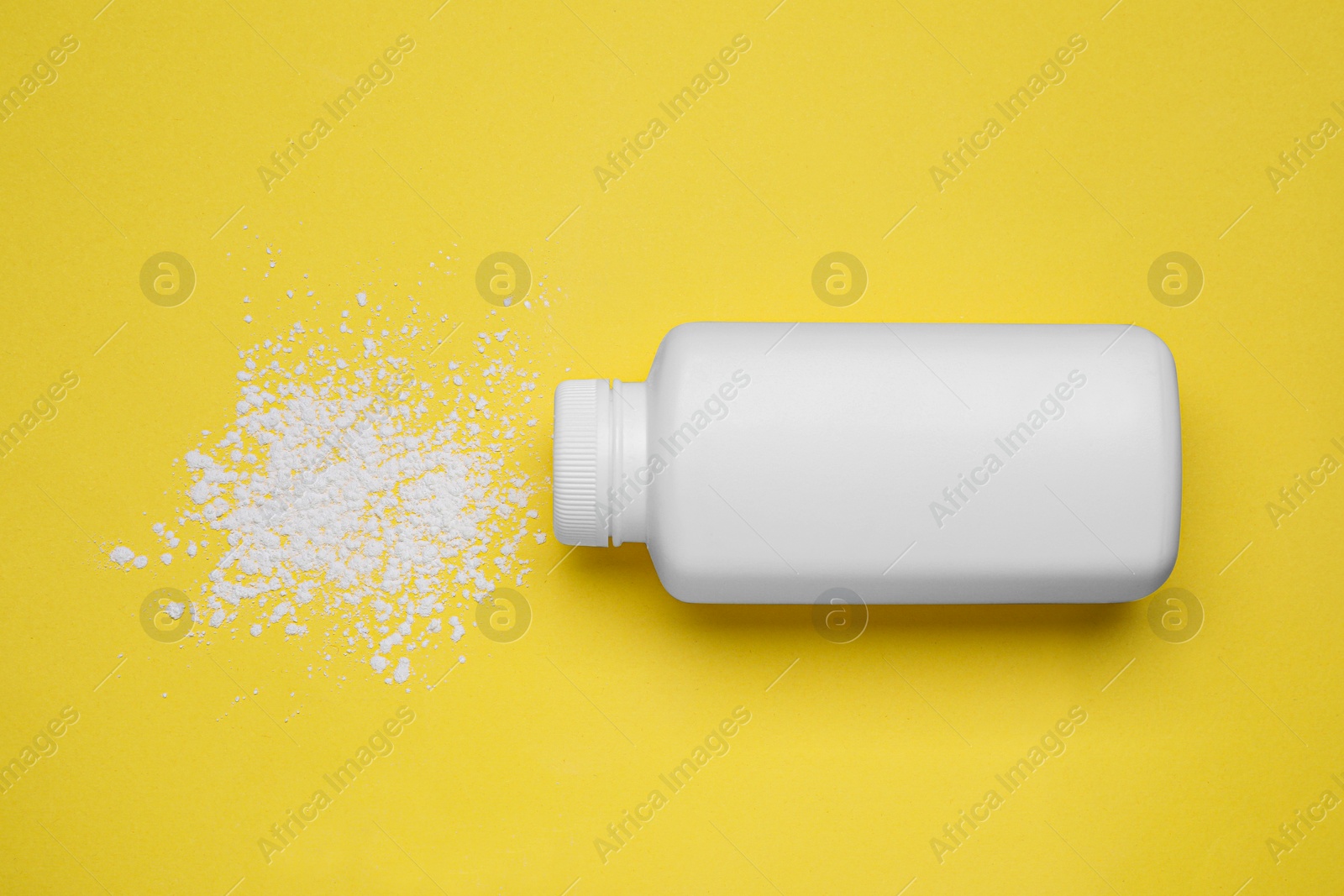 Photo of Bottle and scattered dusting powder on yellow background, top view. Baby cosmetic product