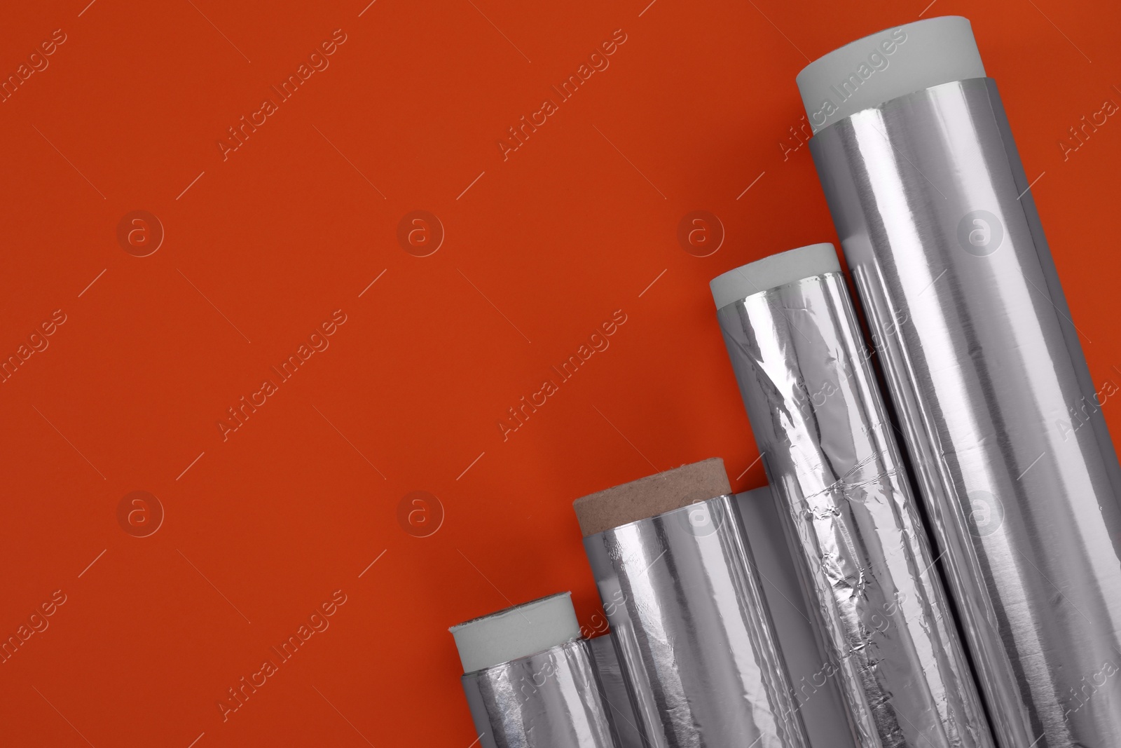 Photo of Rolls of aluminum foil on red background, flat lay. Space for text