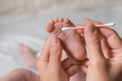 Photo of Mother cleaning baby`s foot with cotton bud on blurred background, closeup
