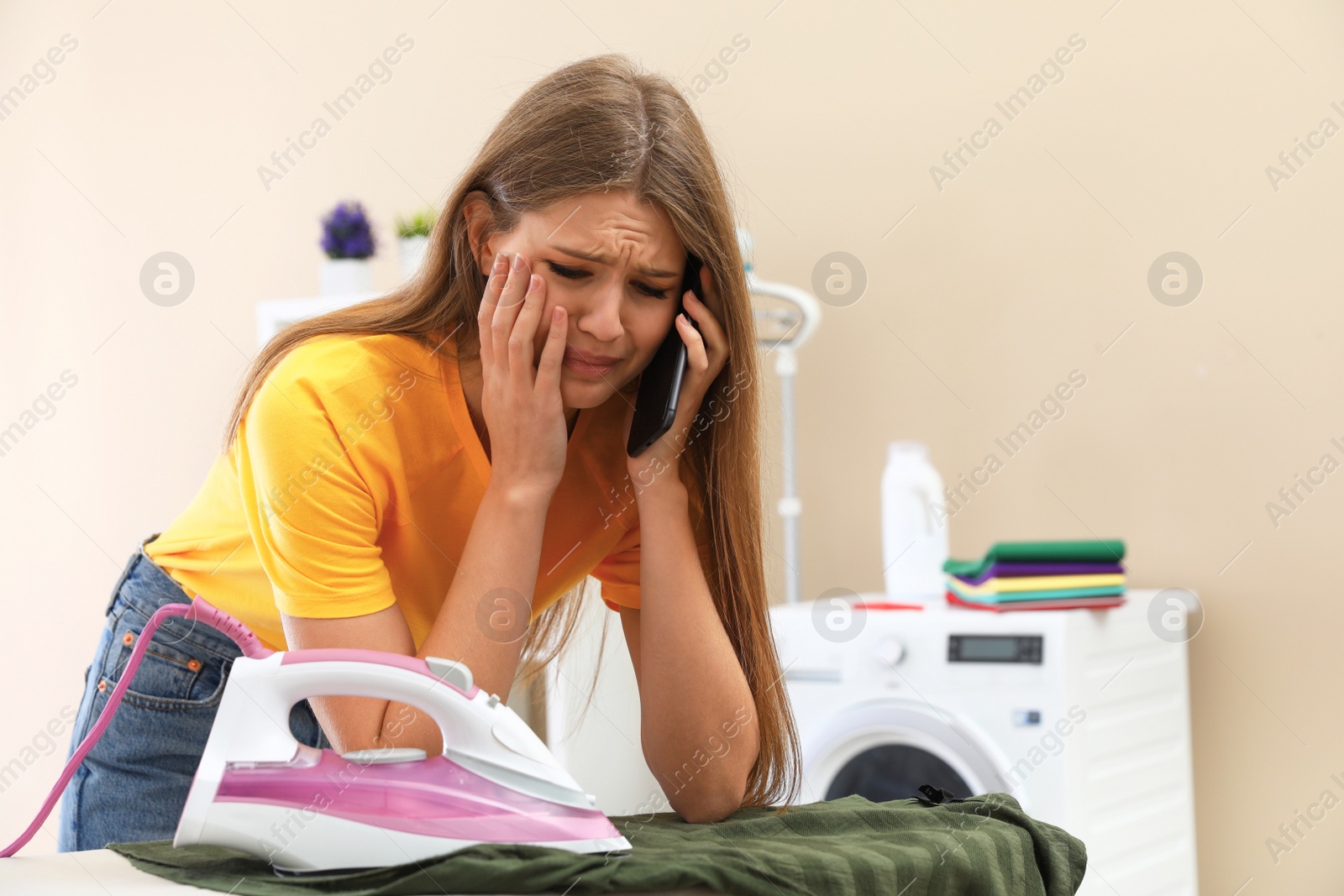 Photo of Sad woman talking on phone while ironing clothes in bathroom. Space for text