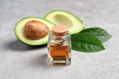 Photo of Bottle of essential oil, fresh avocado and green leaves on grey table