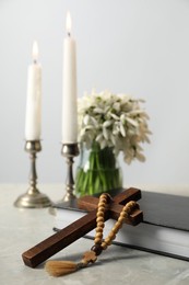 Wooden cross, rosary beads, Bible, church candles and flowers on marble table