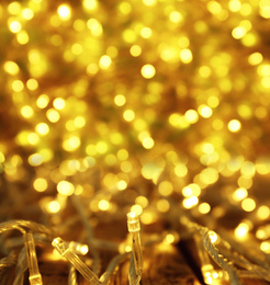 Image of Glowing gold Christmas lights on table, closeup view. Bokeh effect