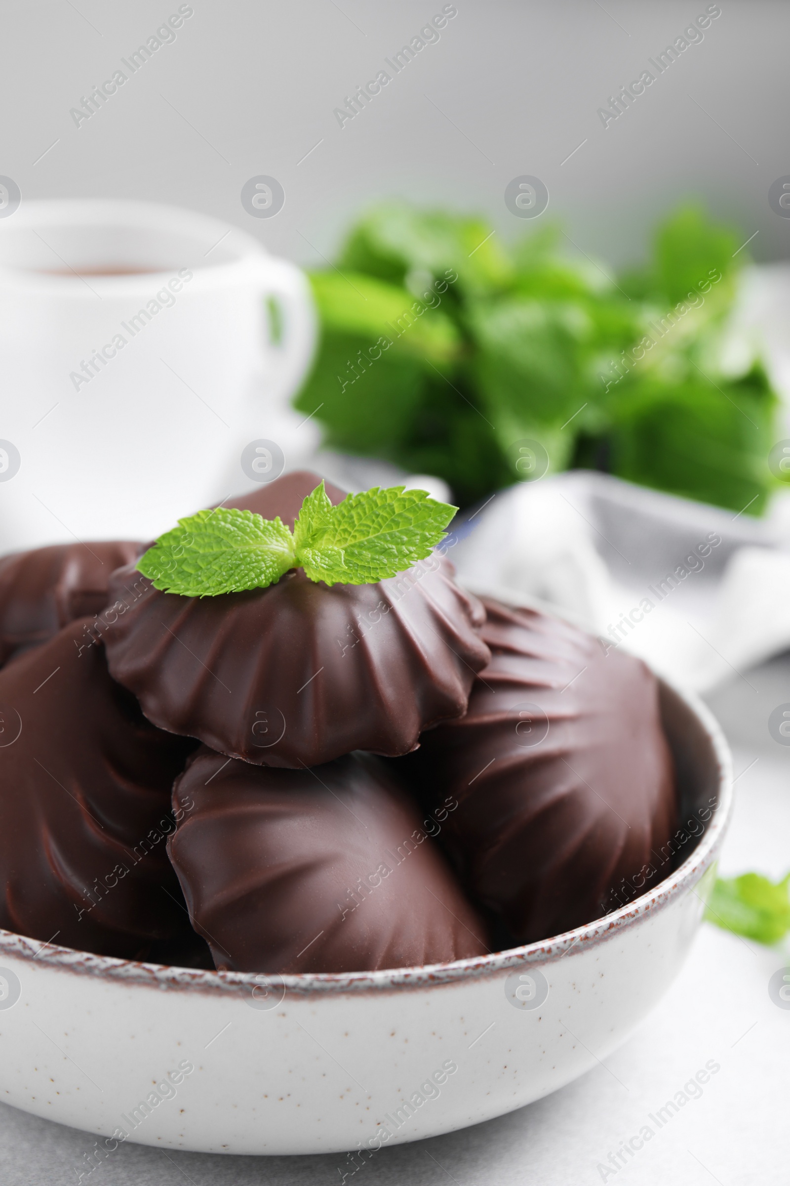 Photo of Delicious chocolate covered zephyrs with mint in bowl on white table, closeup