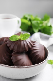 Delicious chocolate covered zephyrs with mint in bowl on white table, closeup