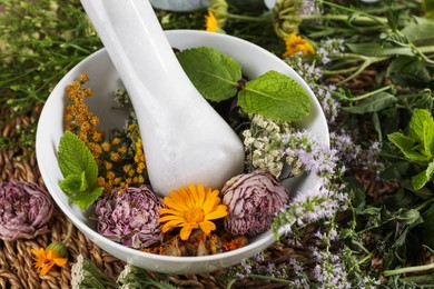 Mortar with pestle and many different herbs on table, closeup