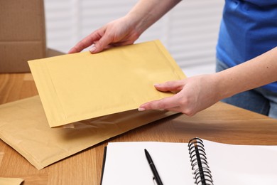 Photo of Post office worker packing parcel at wooden table indoors, closeup