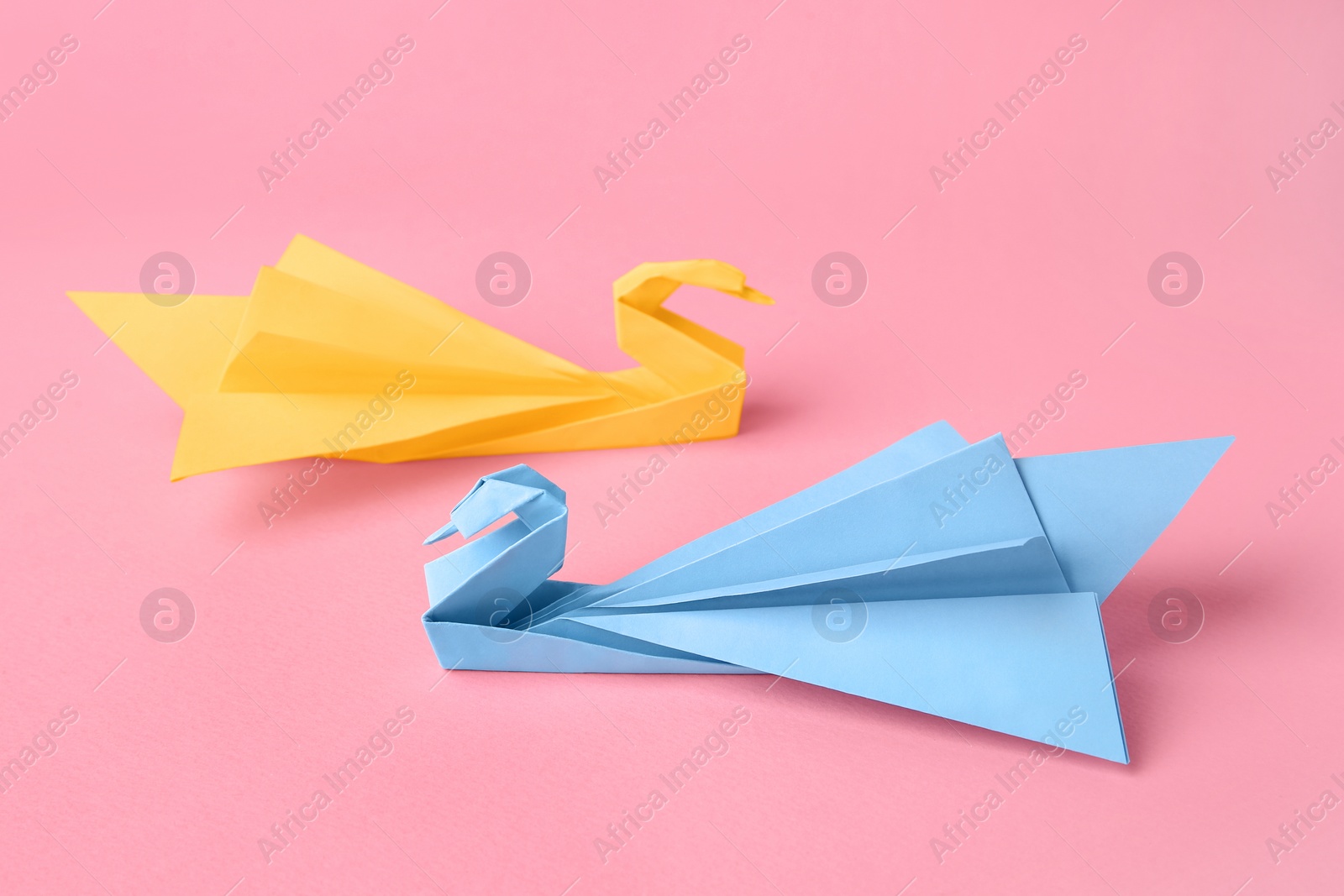 Photo of Origami art. Beautiful paper swans on pink background