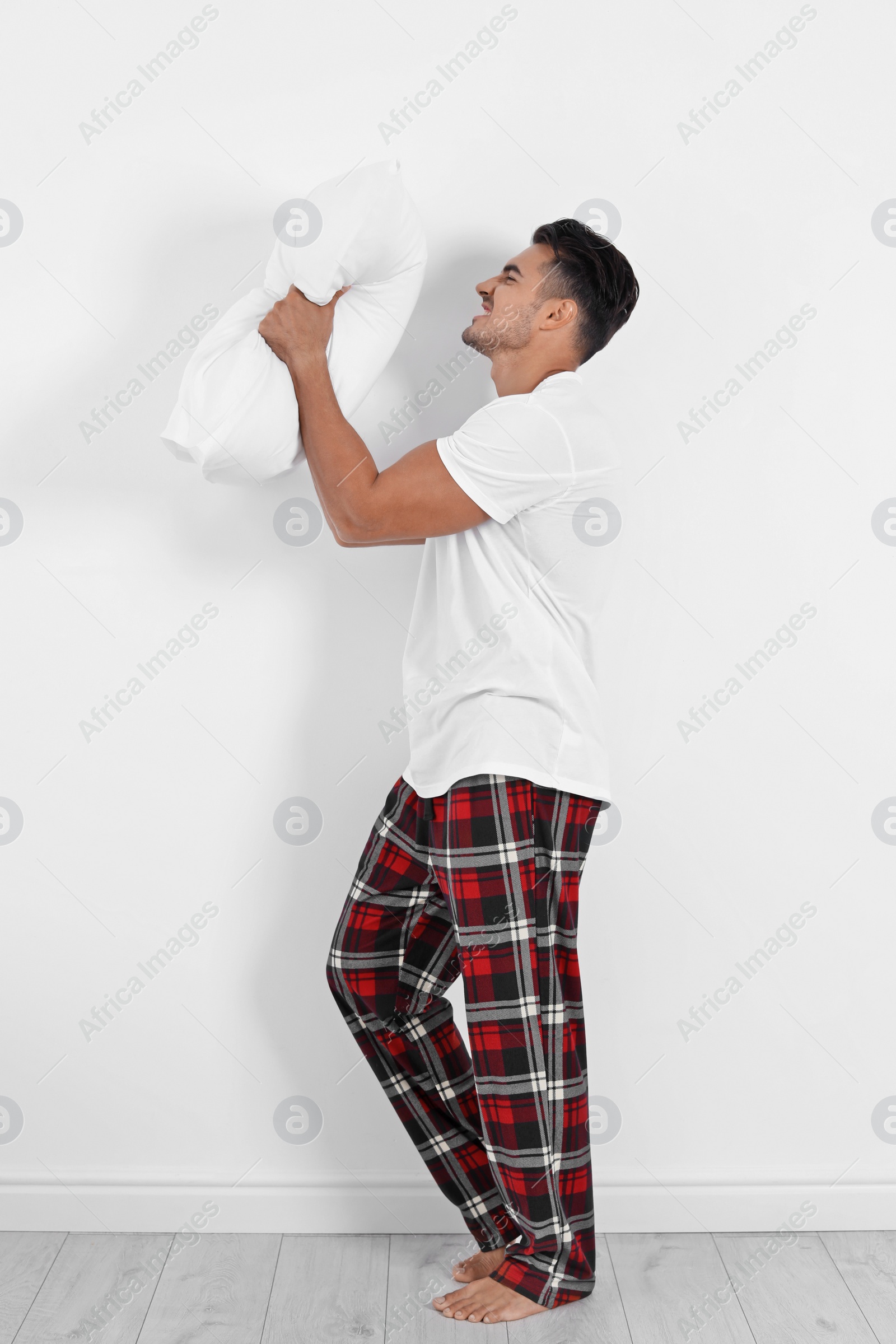Photo of Emotional young man with soft pillow near white wall