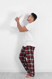 Emotional young man with soft pillow near white wall