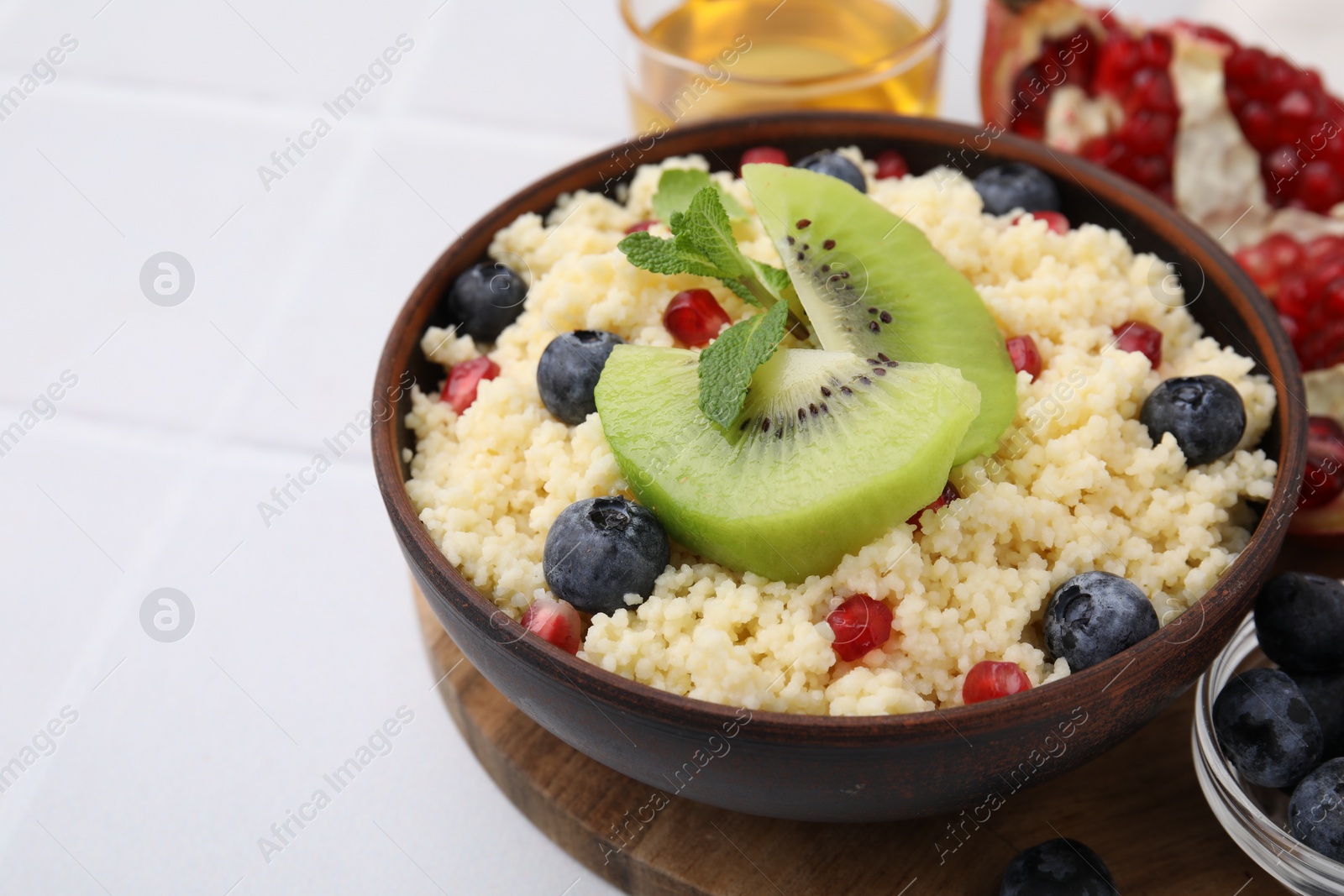 Photo of Bowl of tasty couscous with kiwi, blueberries and pomegranate on white table, closeup. Space for text