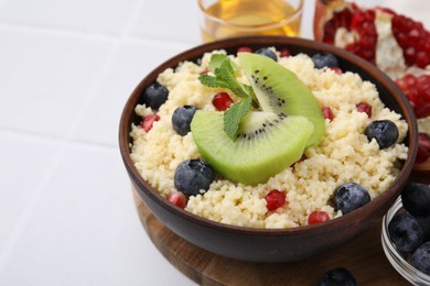 Bowl of tasty couscous with kiwi, blueberries and pomegranate on white table, closeup. Space for text