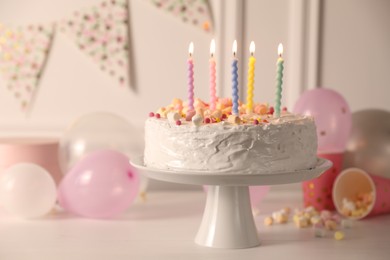 Tasty Birthday cake with burning candles and party decor on white table, closeup