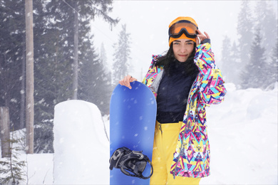 Photo of Young woman with snowboard wearing winter sport clothes outdoors