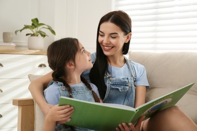 Photo of Young mother and her daughter reading book on sofa at home