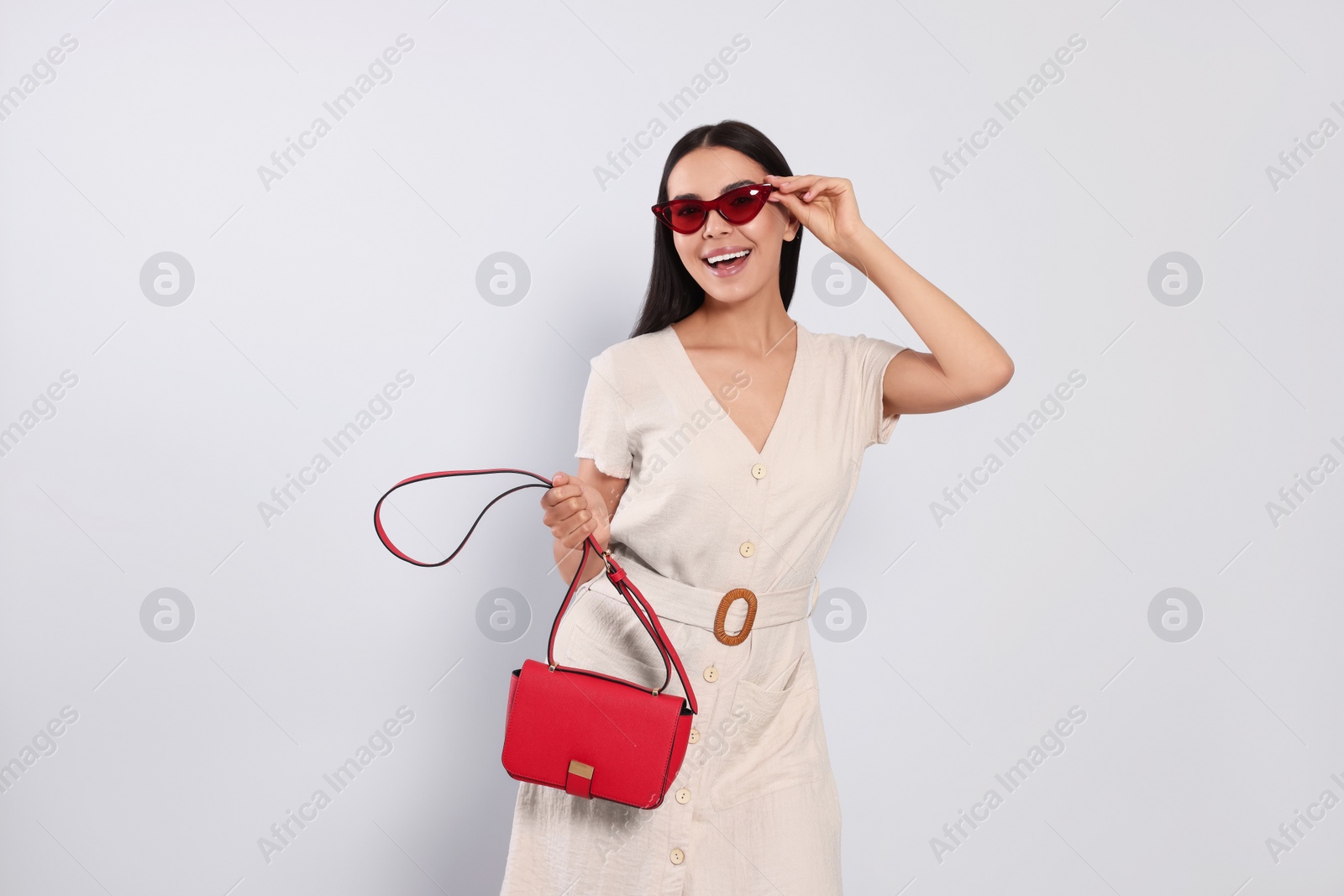 Photo of Beautiful young woman with red bag in stylish sunglasses on light grey background