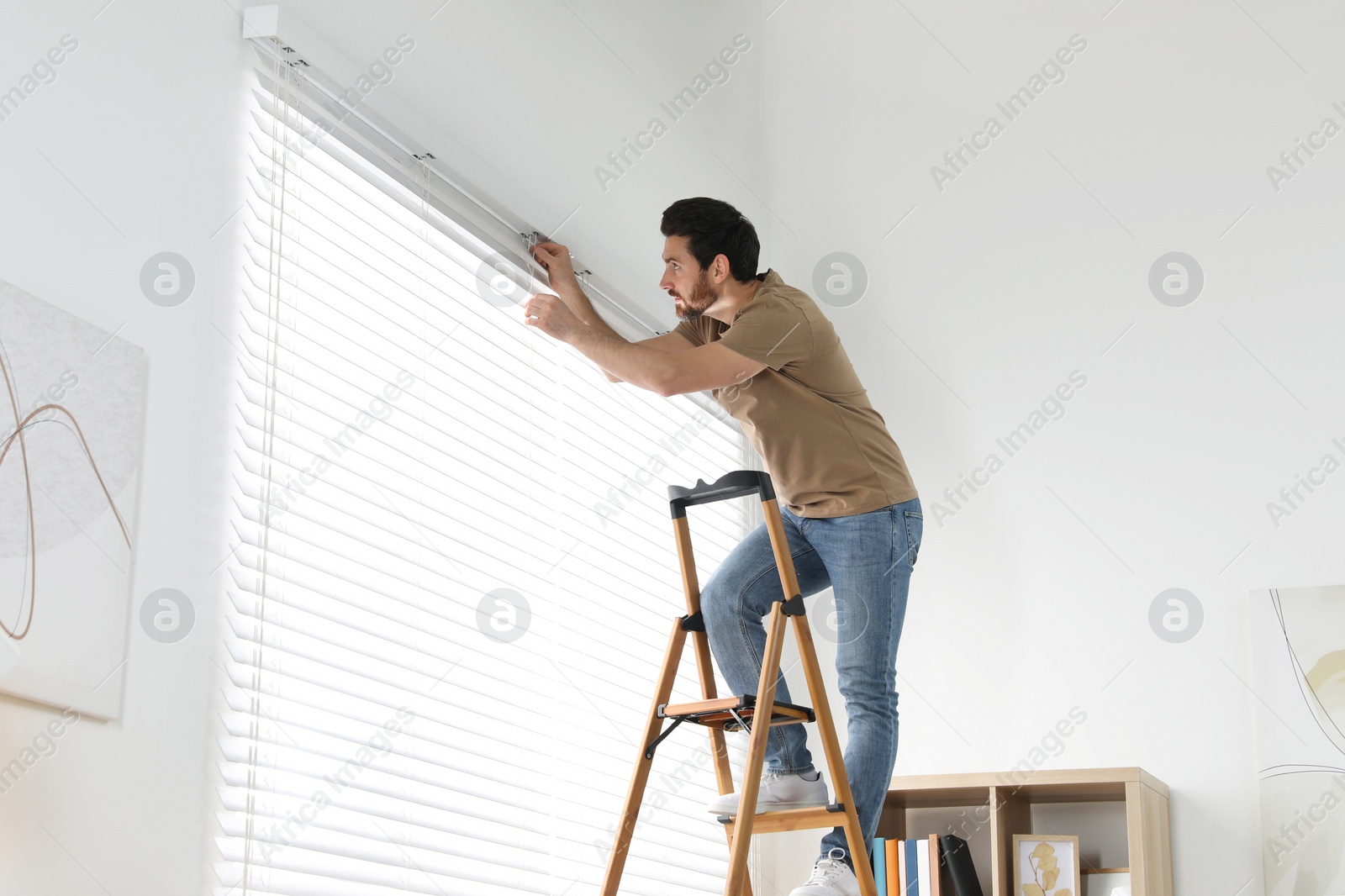 Photo of Man on wooden folding ladder installing blinds at home