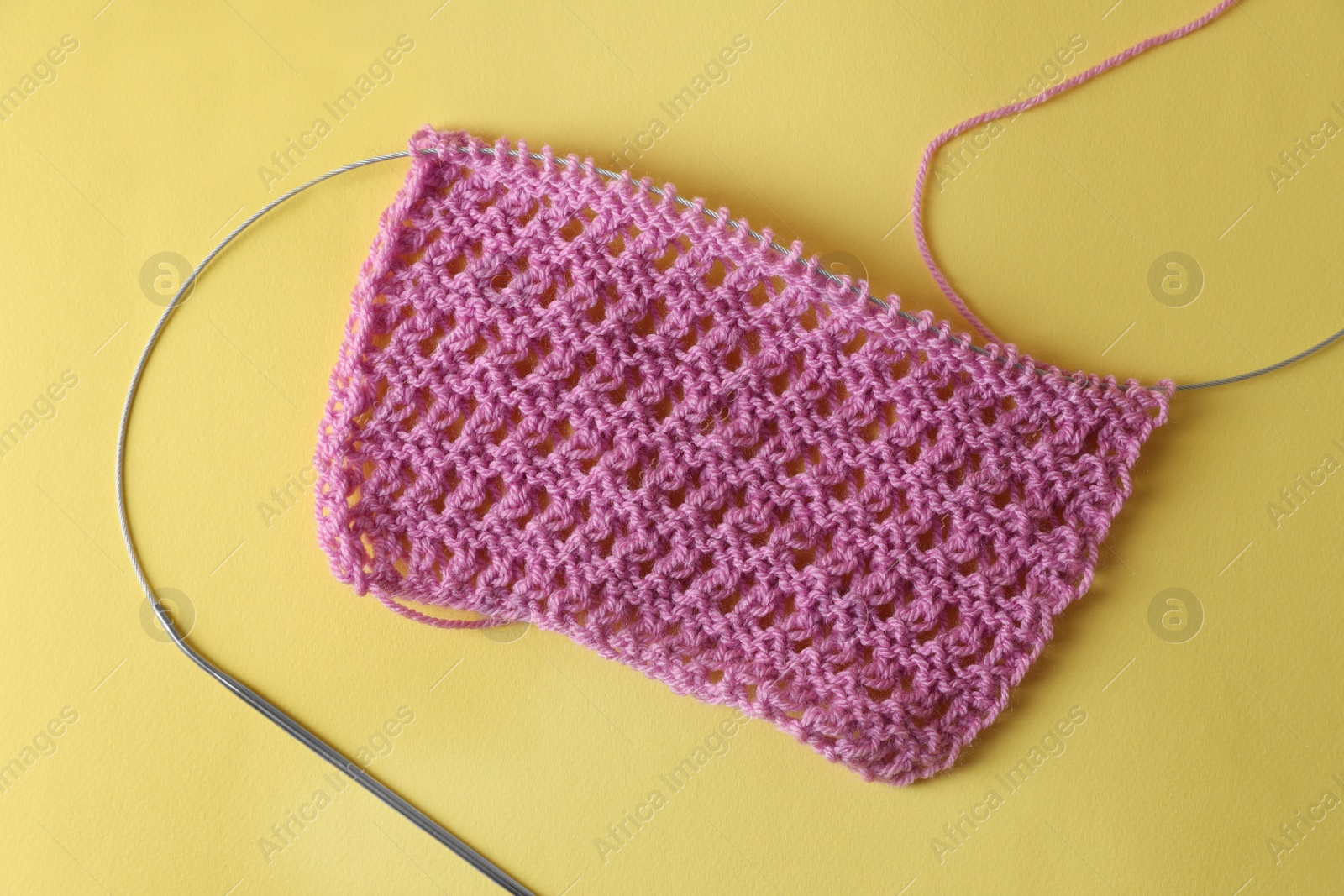 Photo of Pink knitting and needle on yellow background, top view