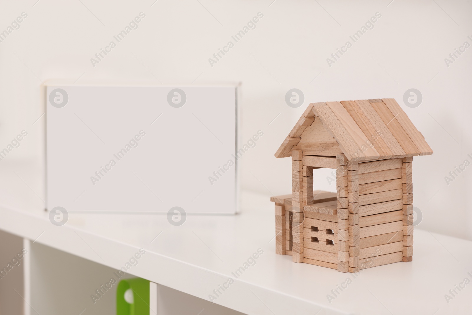 Photo of Wooden house on white shelf indoors, space for text. Educational toy for motor skills development