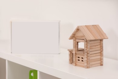 Wooden house on white shelf indoors, space for text. Educational toy for motor skills development