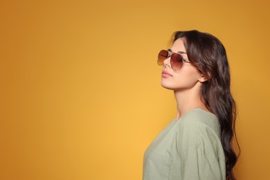 Photo of Beautiful woman with stylish sunglasses on orange background, space for text