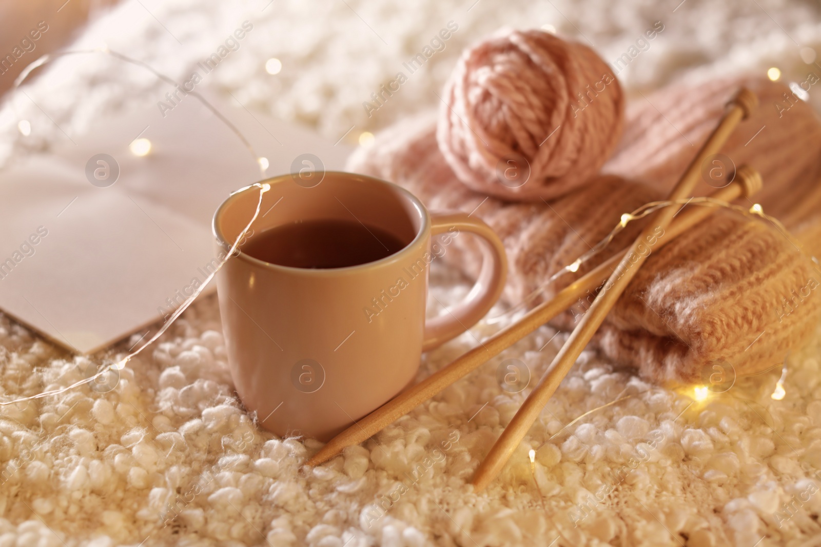 Photo of Composition with cup of hot beverage, knitting yarn and book on fuzzy rug. Winter evening