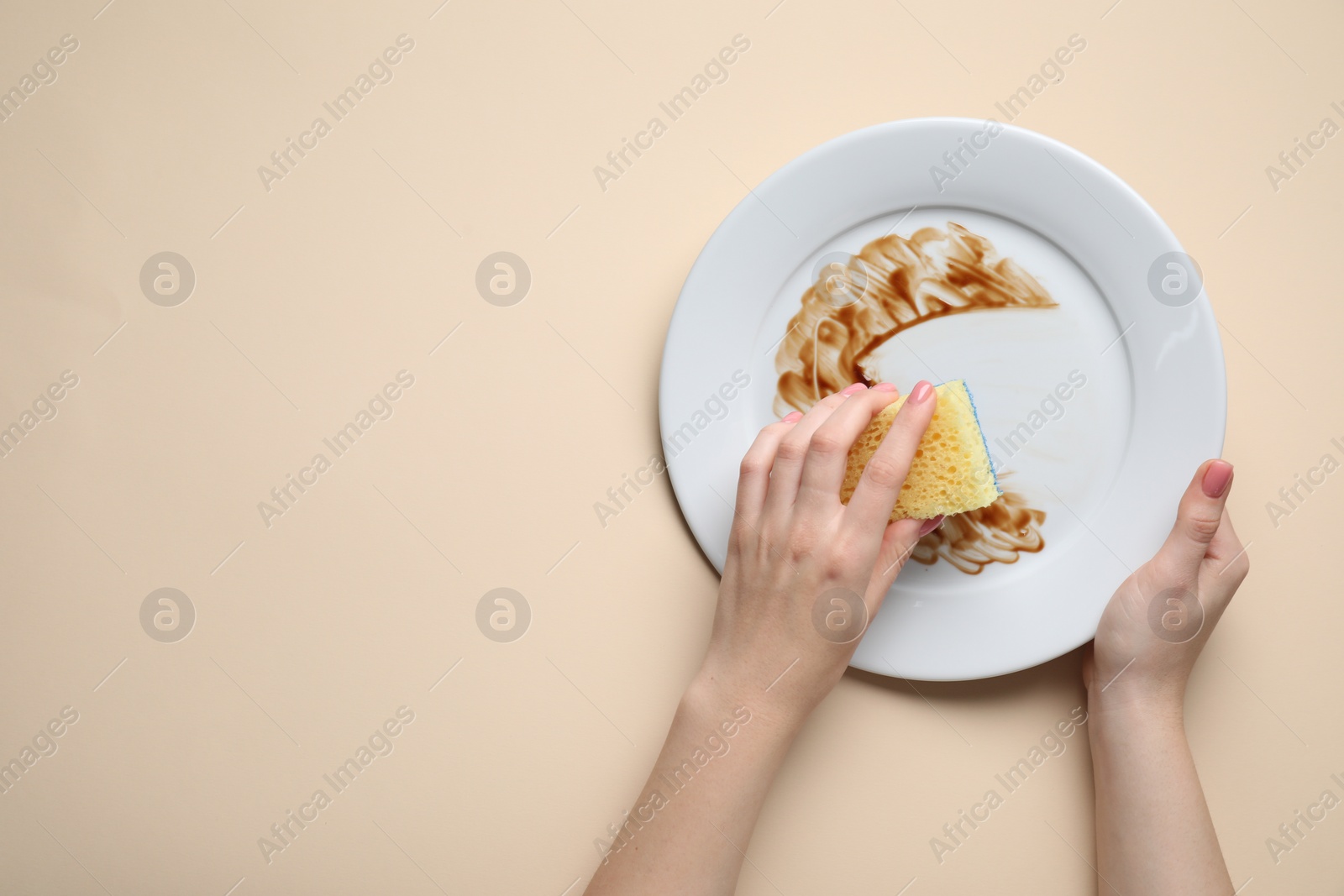 Photo of Woman washing dirty plate with sponge on beige background, top view. Space for text