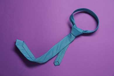Photo of One necktie on purple background, top view