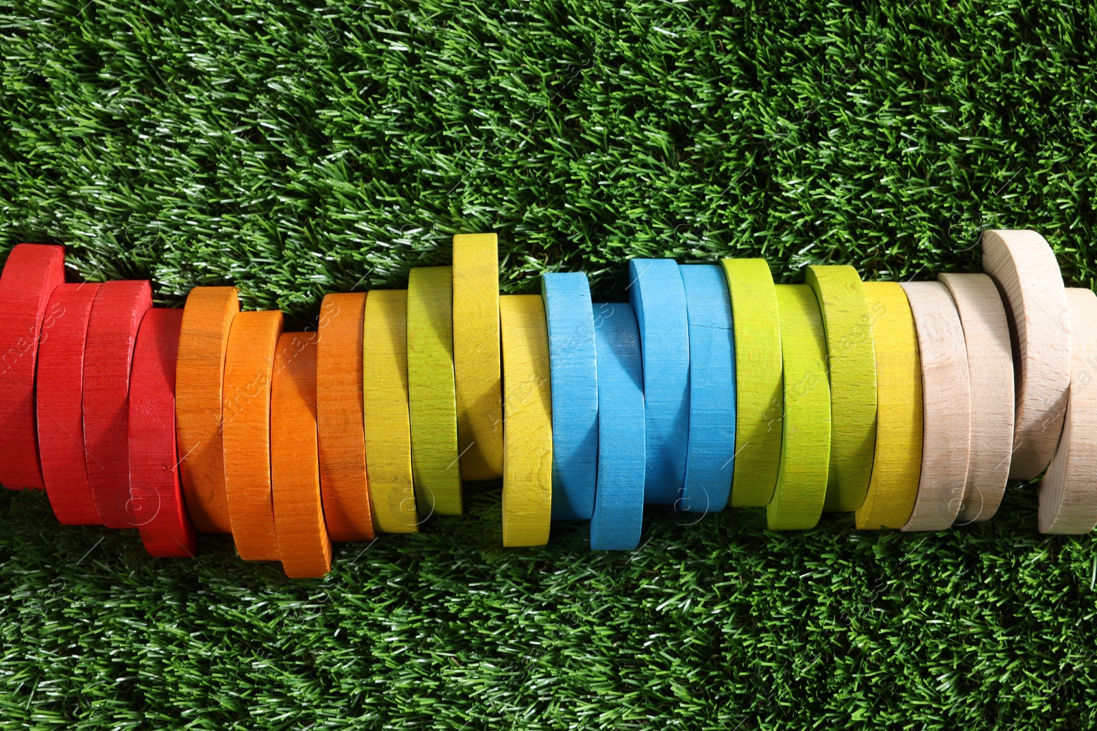 Photo of Colorful wooden pieces of play set on green grass, top view. Educational toy for motor skills development