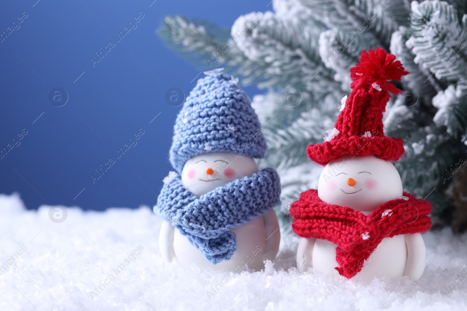 Photo of Cute decorative snowmen and fir tree on artificial snow against light blue background, closeup. Space for text