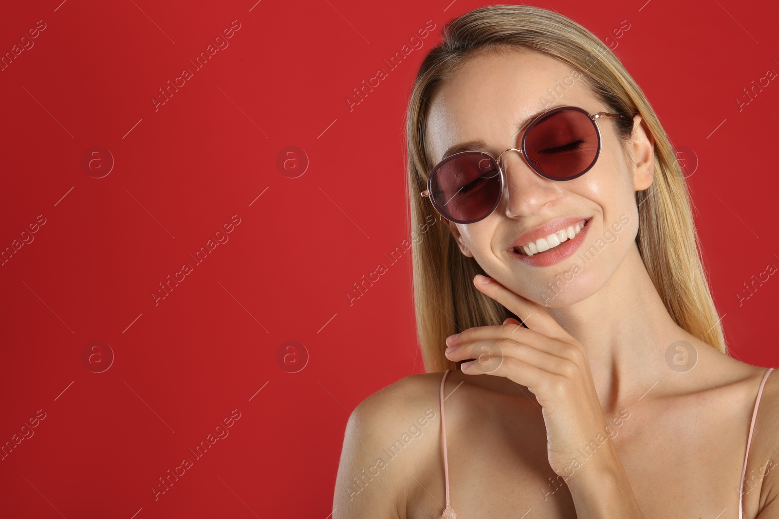 Photo of Beautiful woman in stylish sunglasses on red background. Space for text