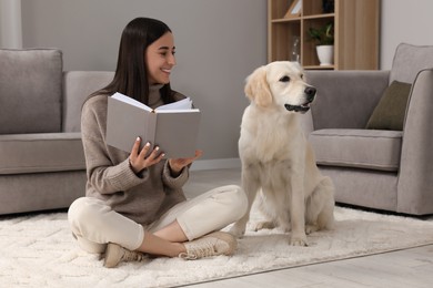 Photo of Happy woman reading book with cute Labrador Retriever dog on floor at home. Adorable pet