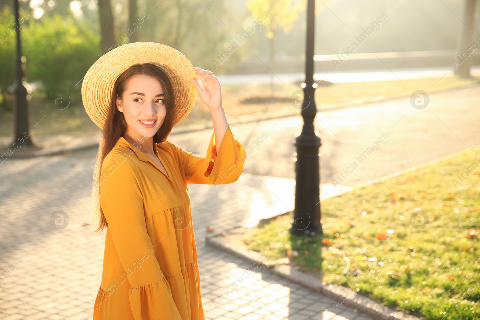 Photo of Beautiful young woman wearing stylish yellow dress and straw hat in park