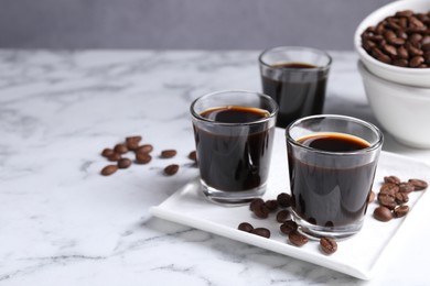 Glasses of coffee liqueur and beans on white marble table, space for text